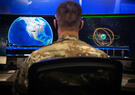 A man in uniform reviews data on two computer screens.