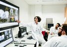 A clinical registrar reviewing a patients test results, looking at some information on a large monitor with some other doctors.