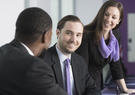 three people in a conference room chatting and smiling