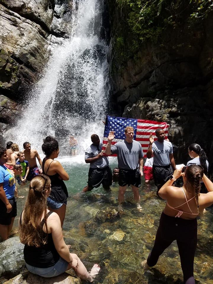 Joseph Alemany standing in front of an American flag at a waterfall