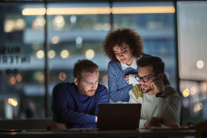 Three technology professionals collaborating around a laptop.