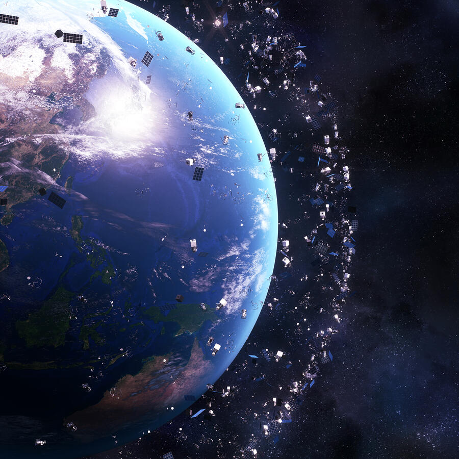 Earth is shown from space surrounded by a dense cloud of satellites and debris orbiting the planet. The scene highlights the crowded environment in Earth’s orbit against a dark starry background.