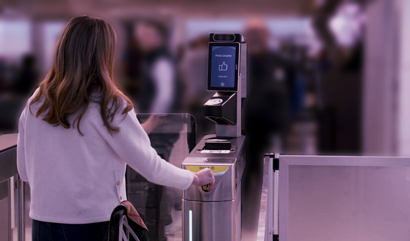 A traveler uses an automated airport eGate, scanning their passport at a self-service checkpoint with a biometric verification screen.