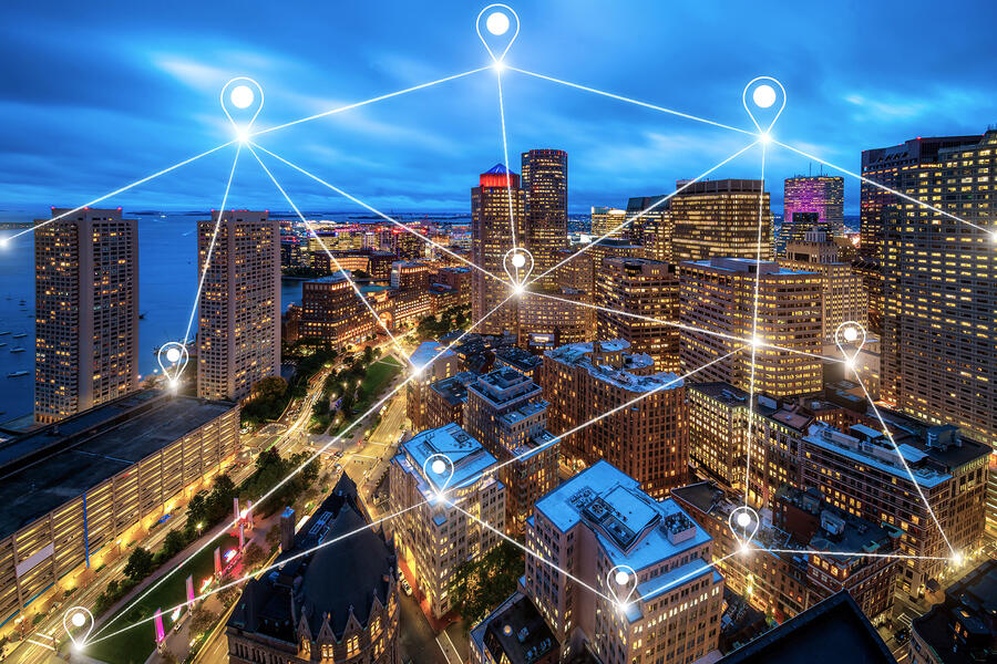 An aerial view of a city skyline at dusk features glowing location markers and connected lines overlaying the buildings, illustrating a digital network across an urban environment.