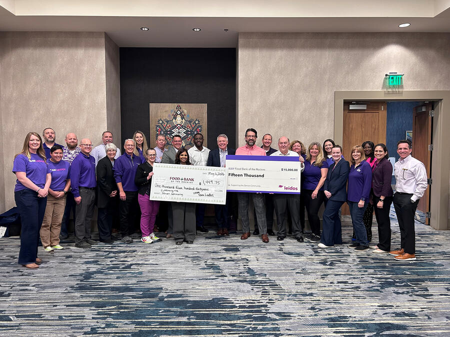 A group of employees stands together indoors holding oversized donation checks for Food Bank of the Rockies during a community fundraising event.