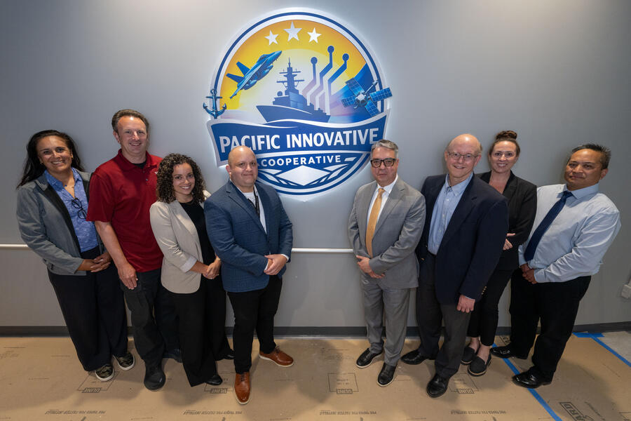 A group of professionals stands together beneath the Pacific Innovative Cooperative logo during a partnership or organizational event.