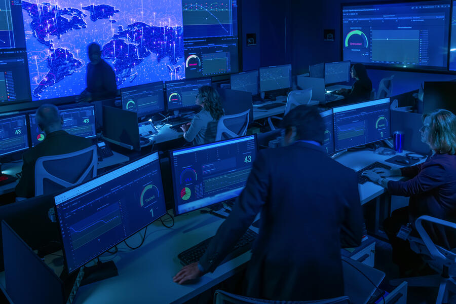 A cybersecurity operations center with analysts monitoring real-time dashboards and global network activity across multiple screens to detect and respond to cyber threats.