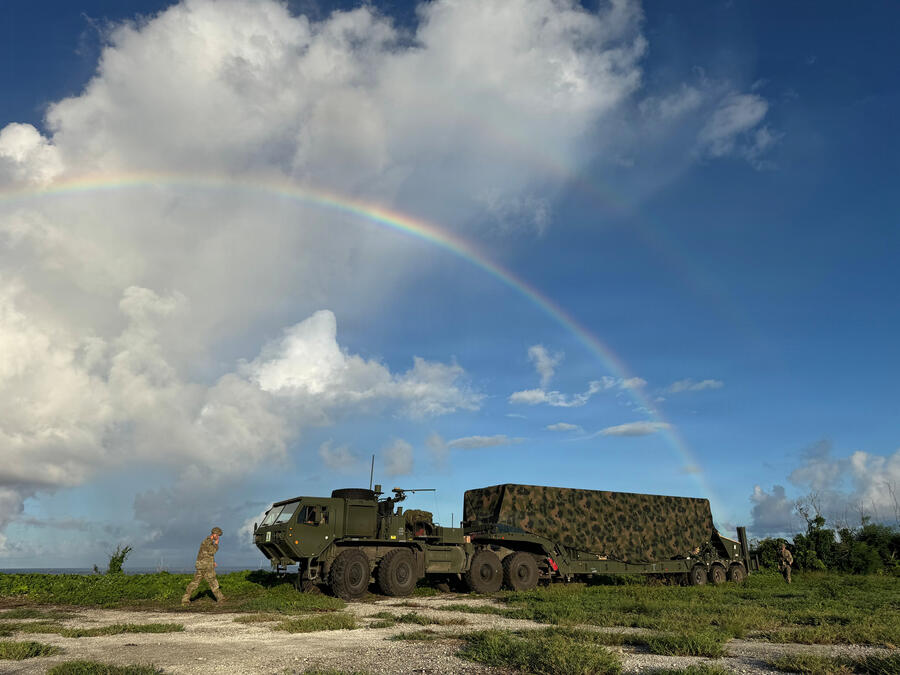 A large military truck on sparse grass with a rainbow in the sky above