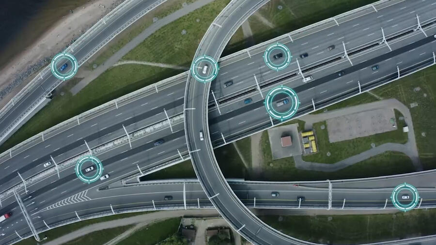 Aerial view of a highway interchange with digital overlays highlighting connected vehicles, illustrating intelligent transportation systems, real-time traffic monitoring, and vehicle-to-infrastructure communication.