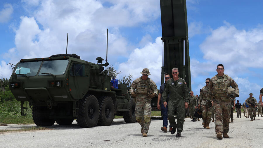 U.S. military personnel and officials walk past a Dark Eagle long-range hypersonic weapon launcher during the Valiant Shield exercise, with the mobile launcher and support vehicle positioned beside the roadway.