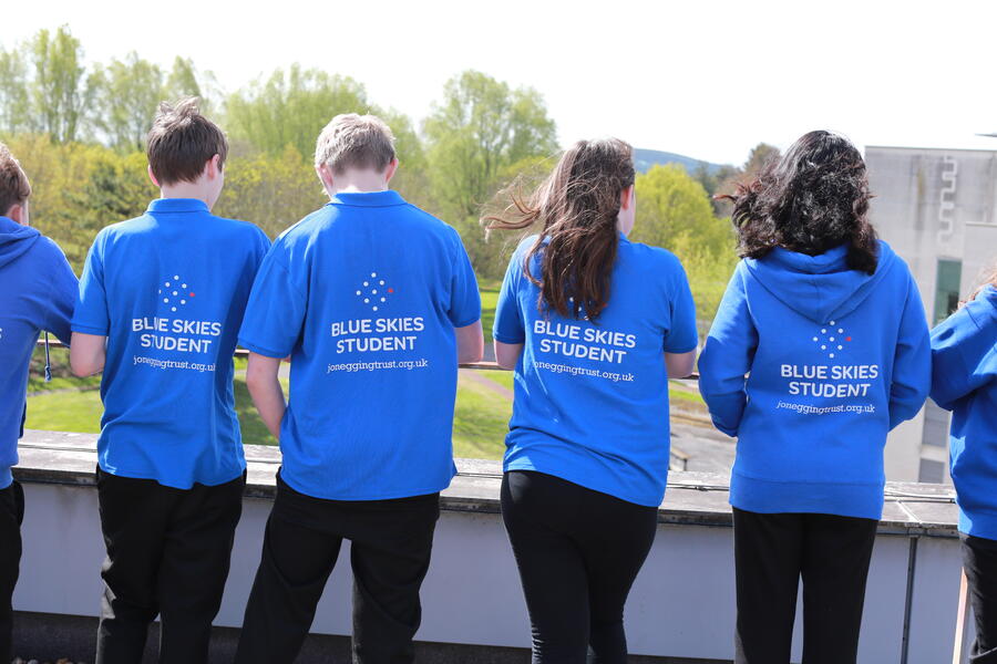 Students wearing Blue Skies programme shirts stand together outdoors, looking across the surrounding landscape during a Jon Egging Trust educational visit.