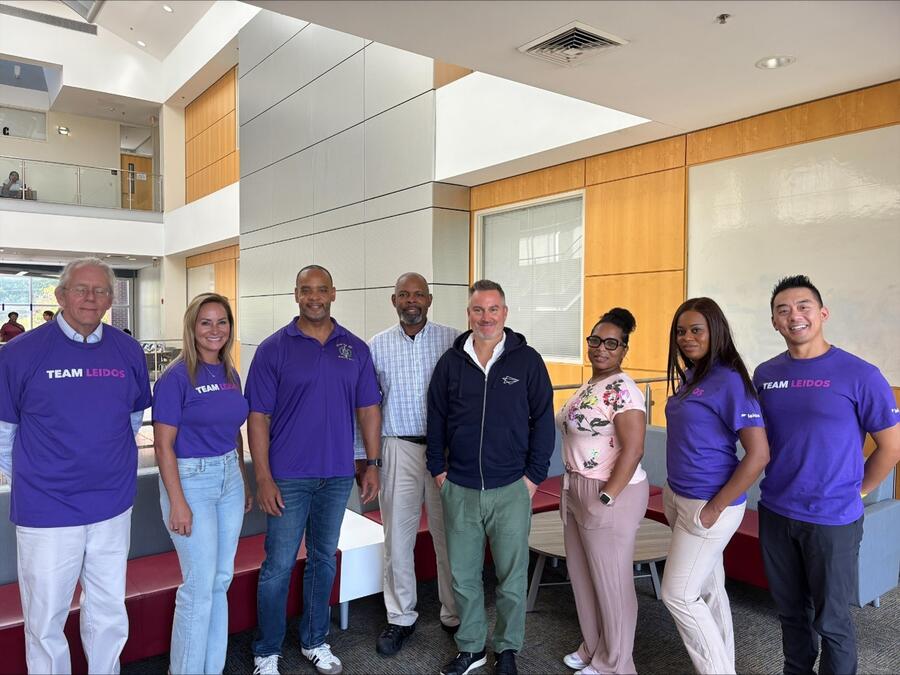 Leidos employees, educators, and community partners pose together in a university building during an AI STEM summer program for high school students.
