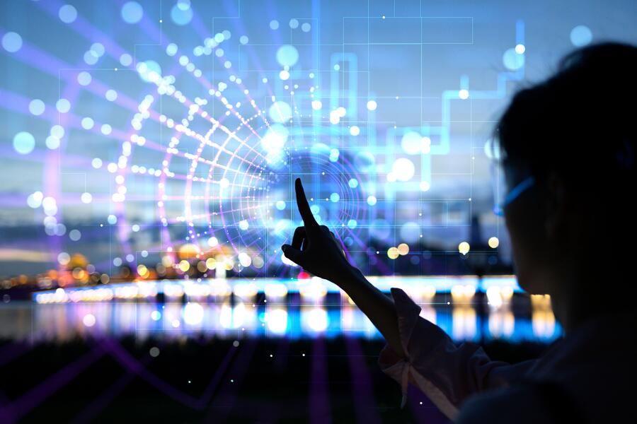 A woman in silhouette pointing at a transparent screen with city lights behind