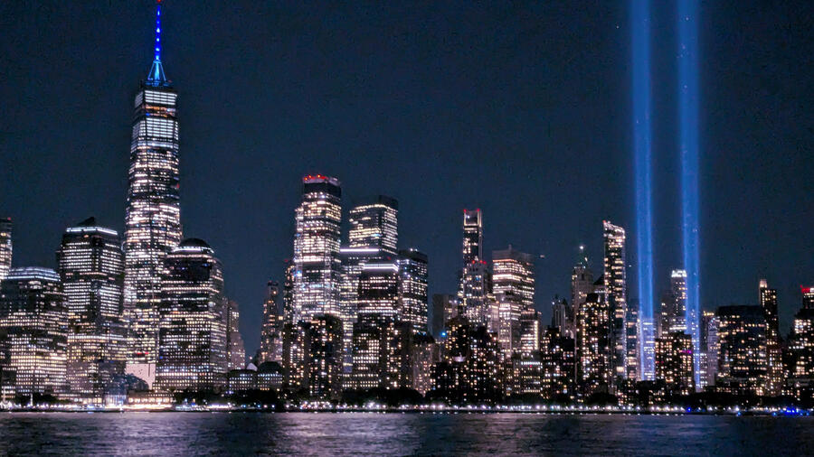 The illuminated New York City skyline at night, with the Tribute in Light beams rising into the sky beside Lower Manhattan.