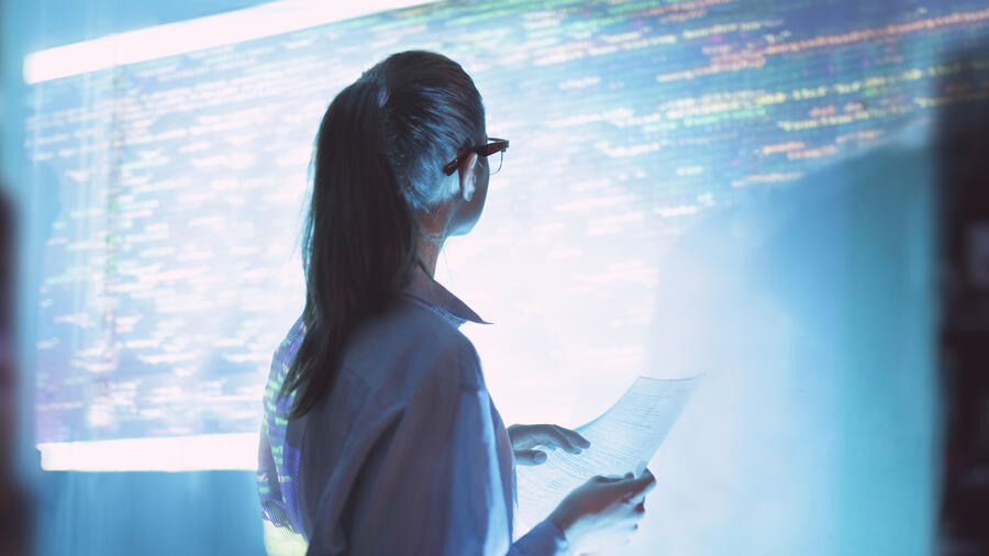 Cybersecurity professional reviews information in front of a large screen displaying computer code.