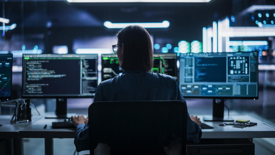 Woman sitting at a computer desk in front of three monitors
