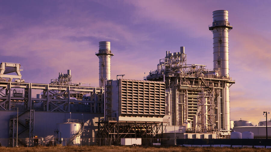 Industrial power plant with tall exhaust stacks, cooling equipment and interconnected pipes against a purple and pink sunset sky.