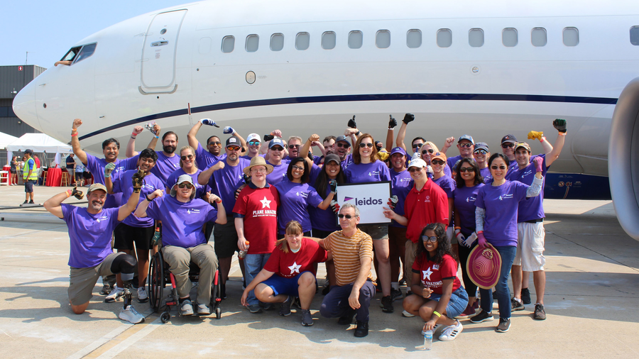 Leidos employees and volunteers from Special Olympics Virginia pose in front of an airplane at the 2022 Dulles Day Plan Pull. 