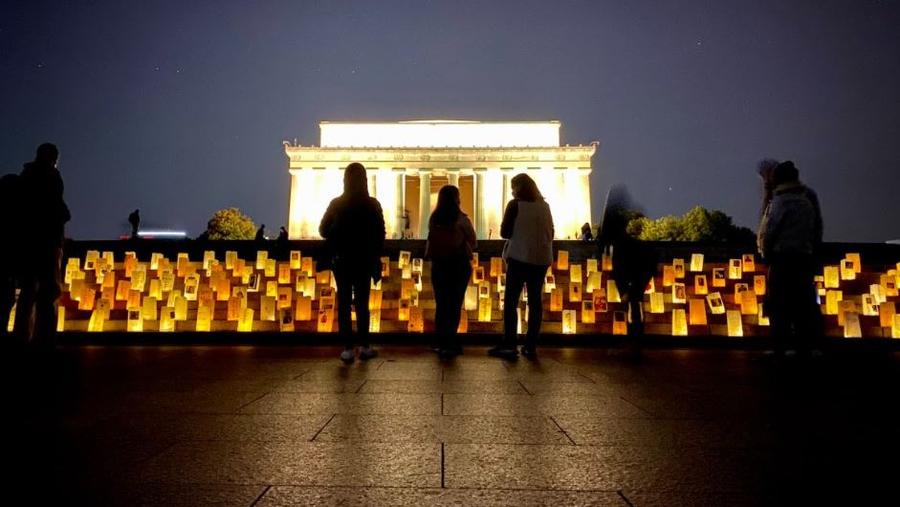 Volunteers stand over lanterns in front of the Lincoln Memorial at dusk