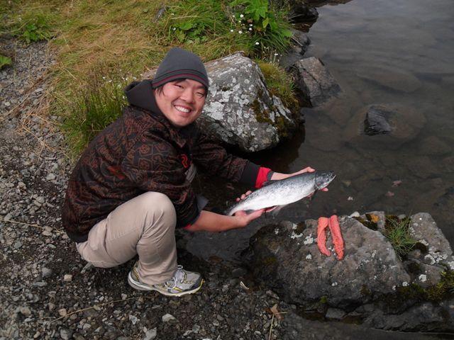 Adak tribe member holding a salmon and smiling at camera