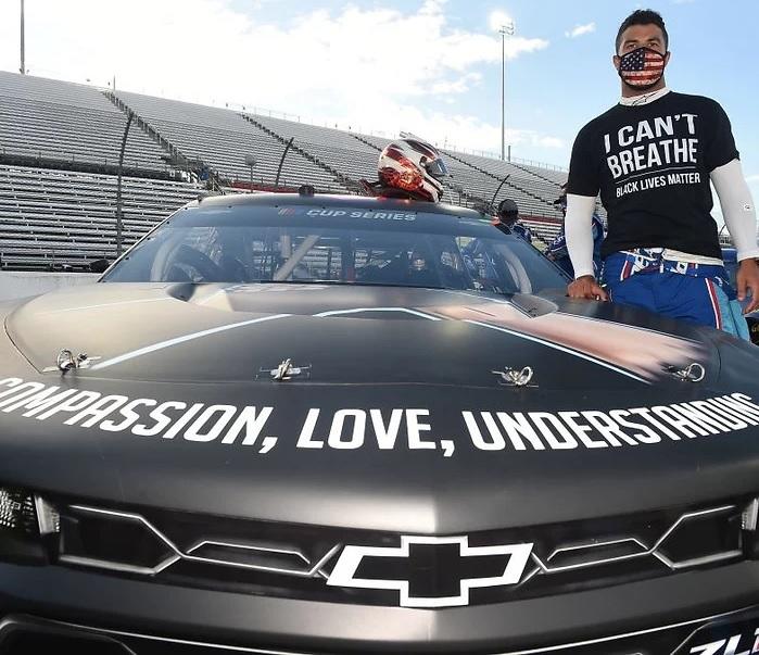 Bubba Wallace poses with a car displaying the message "compassion, love, understanding"