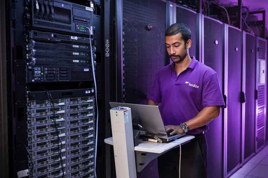 Man typing on a laptop while standing next to server