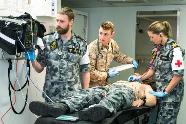 Medical staff in army uniforms attending to patent lying on bed