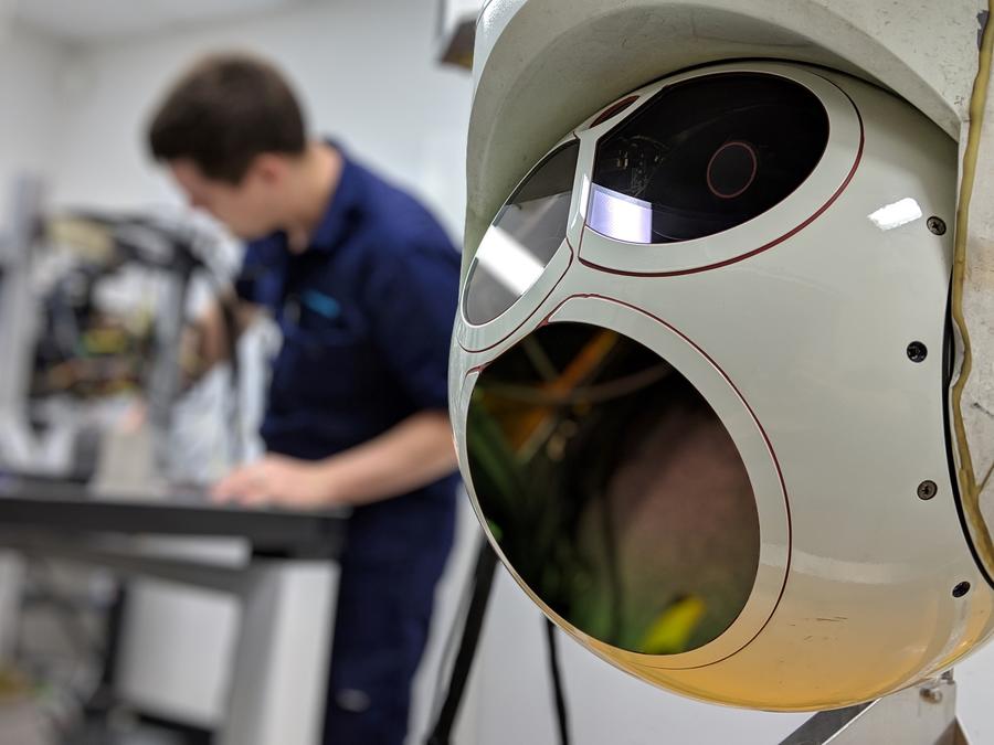 Turret camera in foreground with man working in the background