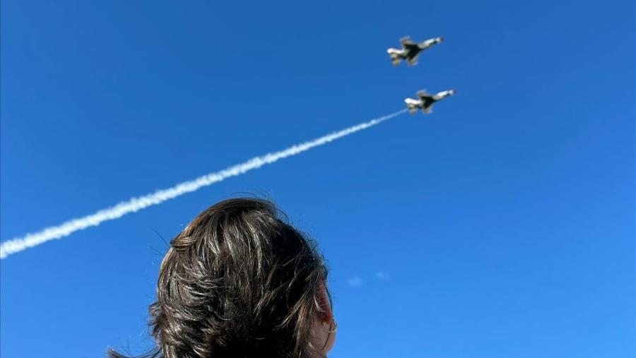 A Leidos employee looks up at the sky with two aircraft flying overhead 