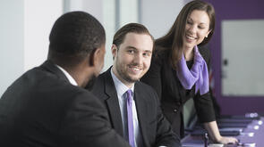 three people in a conference room chatting and smiling