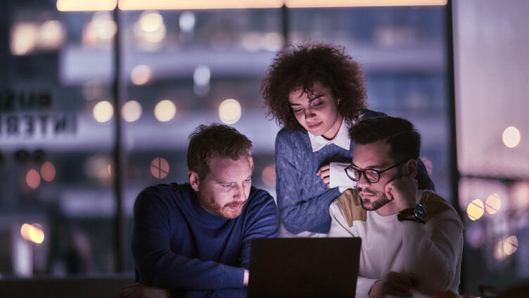 Three technology professionals collaborating around a laptop.