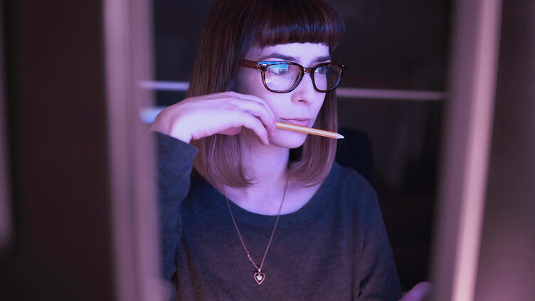 Woman sitting at computer holding a pencil