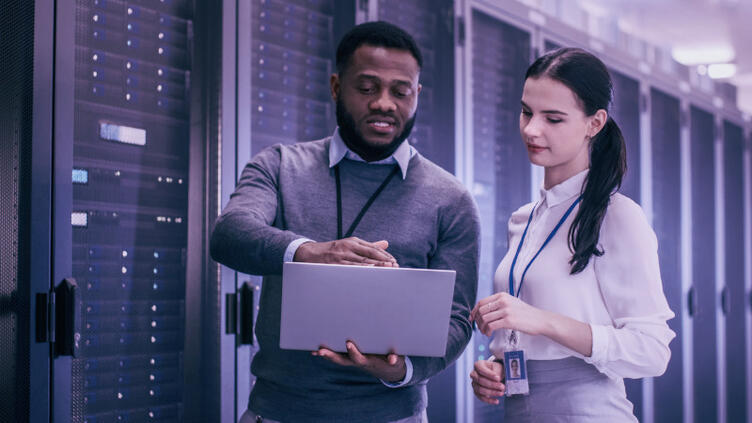 Two people look at a laptop in a data center