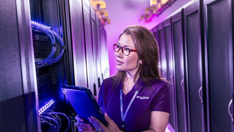 woman holds tablet while looking at server rack
