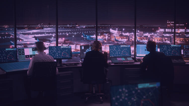 three employees facing monitors in a control tower