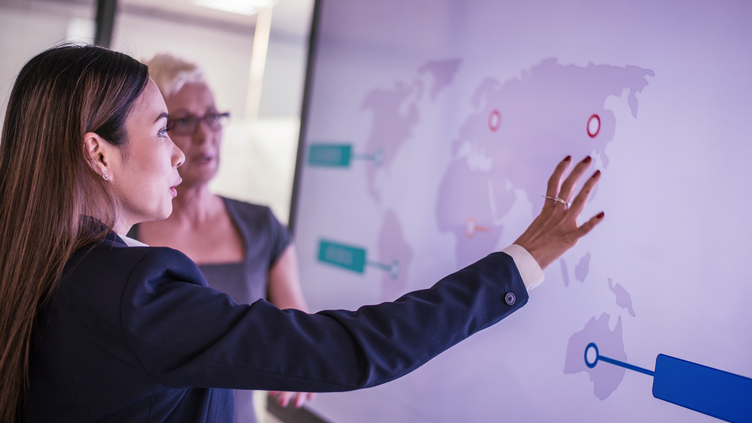 woman in navy blue suit jacket standing in front of a white screen of a digital map 