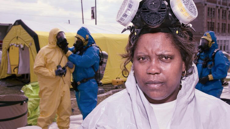 A woman in a hazmat suit faces the camera while other people in different coloured hazmat suits are behind her.