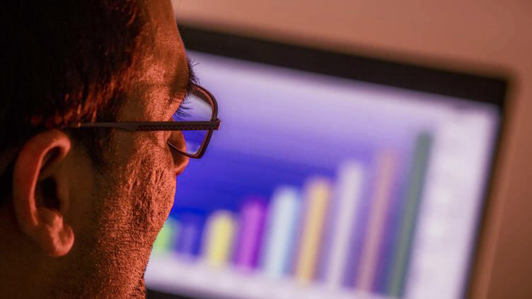 A sideview of a man with glasses looking at a computer screen with a graph on it