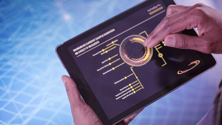 A tablet is held with two hands in front of a screen