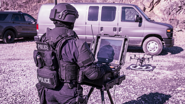 Person in tactical police uniform piloting a drone from a laptop