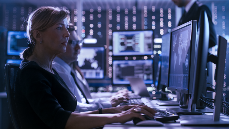 a man and woman sitting in front of multiple computer monitors