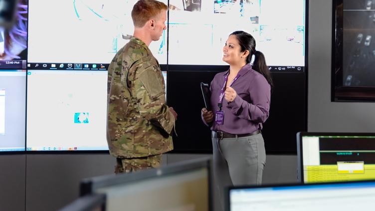 two coworkers talking in-front of screens with data on them