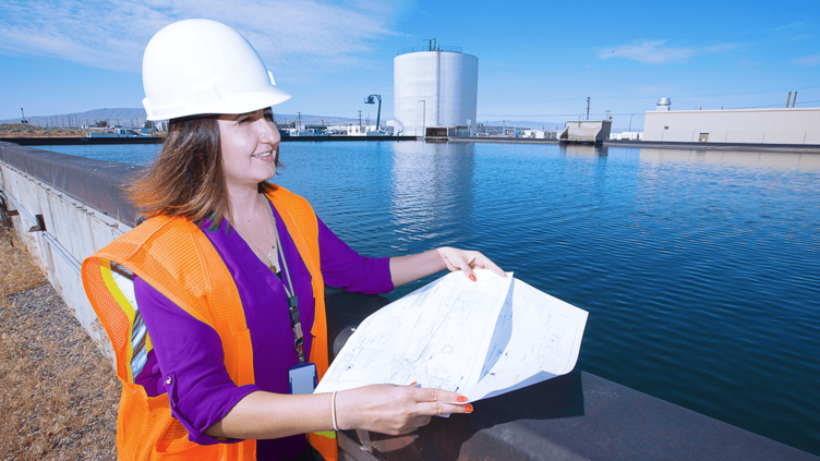 A female worker gazes over a reservoir while holding detailed diagrams