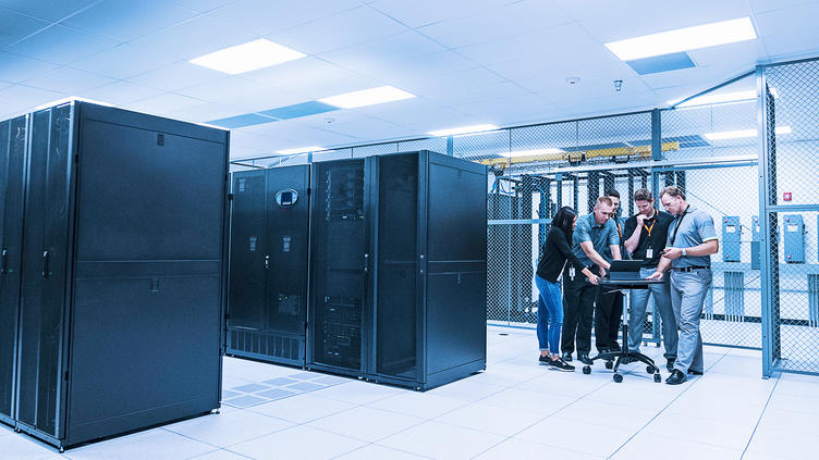 four coworkers standing at laptop next to server racks