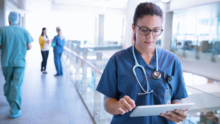 Nurse with stethoscope around her neck walking with tablet
