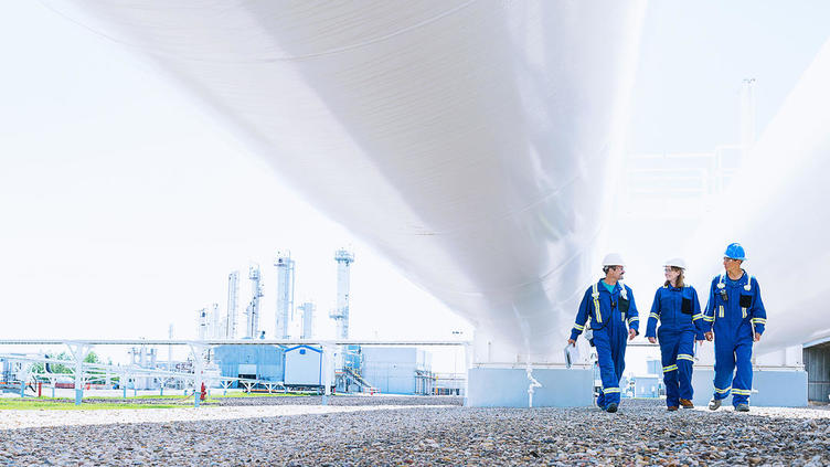 three engineers walking under a large pipe with protective suits on
