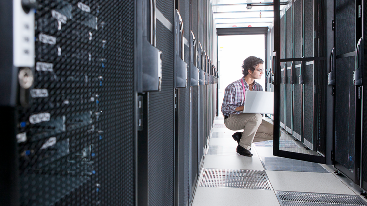 man in server room squatting down with laptop