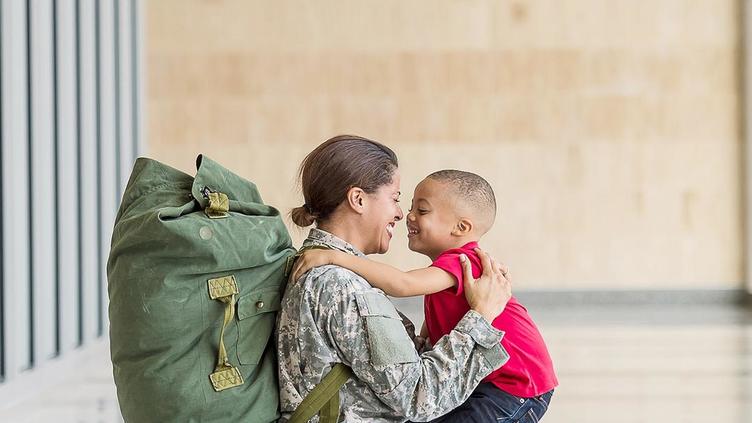 Mother in military uniform embraces her young son