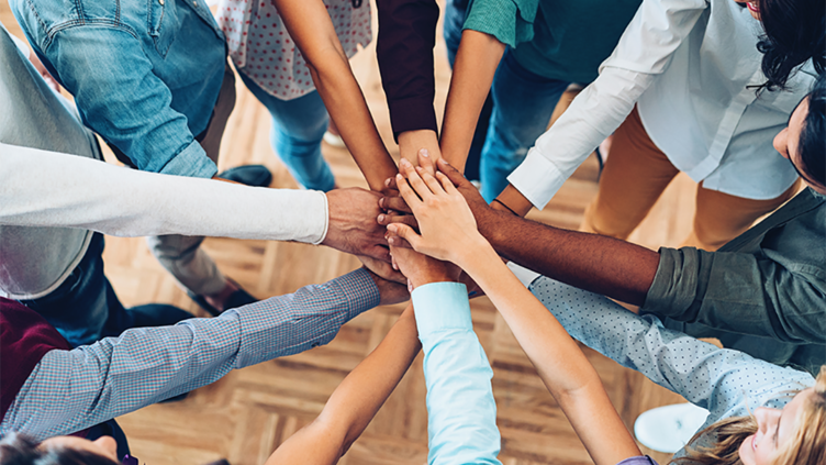 A group of people stood in a circle all with one hand in the middle