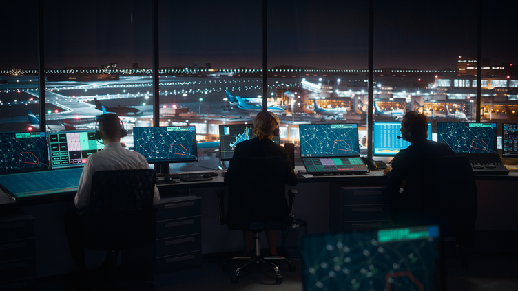 three employees facing monitors in observation tower